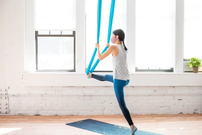 Woman doing aerial yoga standing splits. 