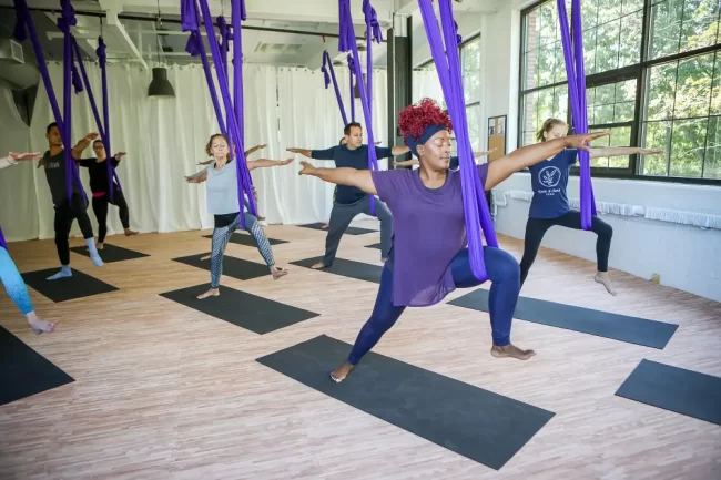 People doing aerial yoga Warrior 2 pose.