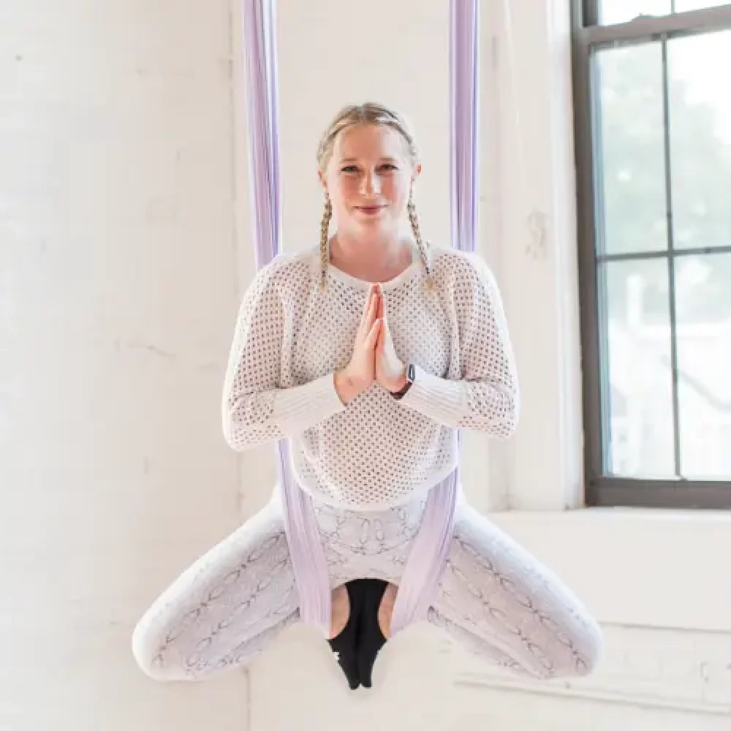 Aerial Yoga Instructor showcases a meditative Buddha pose supported by their hanging aerial silk at Earth & Aerial Yoga located in Hudson MA.