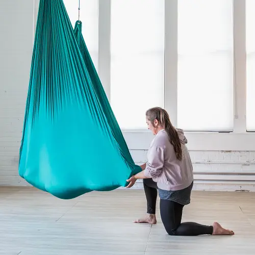Person resting in aerial yoga hammock and a woman holding their feet performing Reiki healing