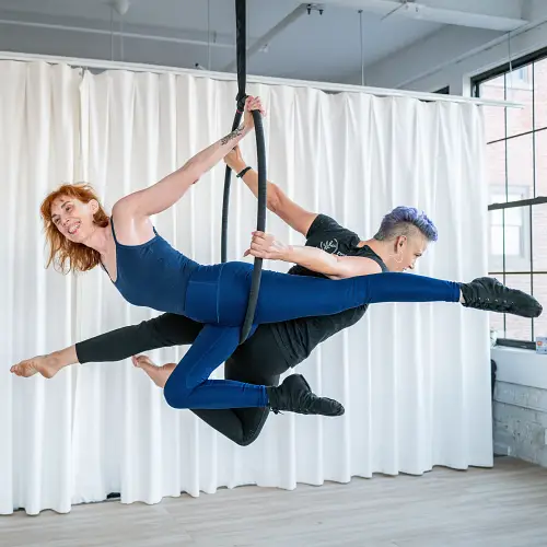 Two women doing a partner aerial hoop pose