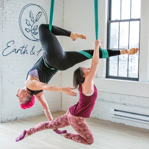 Two women practicing aerial yoga partner poses at Earth & Aerial Yoga